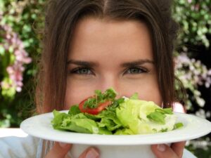 Foto de uma mulher segurando um prato com muitas folhas verdes, próxima ao rosto.
